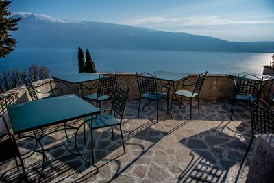 Empty chairs and table by sea against sky