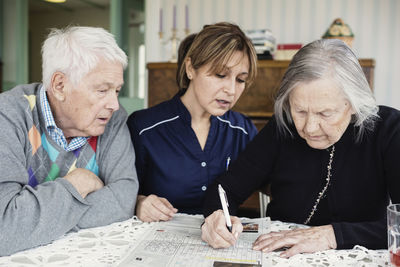 Caretaker assisting senior woman in solving crossword puzzle at nursing home