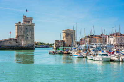 Sailboats in sea by buildings against sky