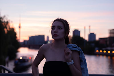 Young woman looking away while standing outdoors during sunset