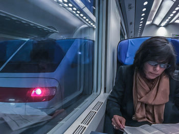 Woman reading book while traveling in illuminated train