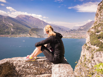 Woman sitting on rock looking at mountains against sky