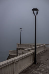 Street light by bridge against sky at dusk