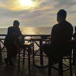 People sitting on table by sea against sky during sunset