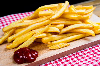 French fries with ketchup on cutting board against black background