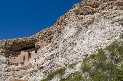 Low angle view of rocky mountain against clear blue sky with ancient buildings in caves.