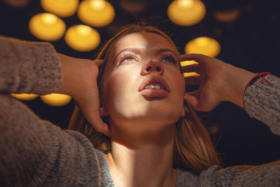 Close-up of young woman looking up against illuminated lighting