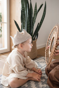 Cute baby girl in crown looks in mirror with love and interest.