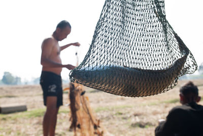 Close-up of fish in net against men on field