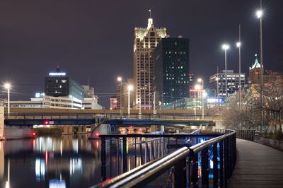 Illuminated bridge over river by buildings against sky at night