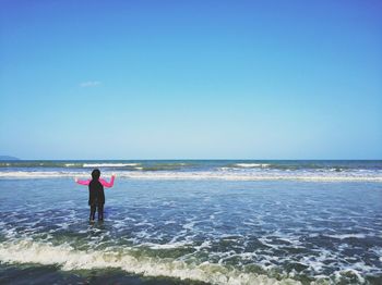 Rear view of man standing on beach against clear sky