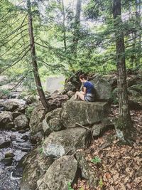 Woman sitting on rock by tree in forest