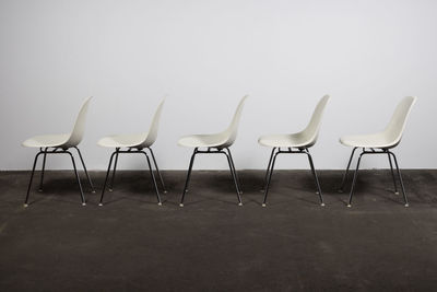 Empty chairs and table against white wall