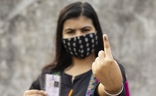 Selective focus on ink-marked finger of an indian woman with safety face mask and voter card