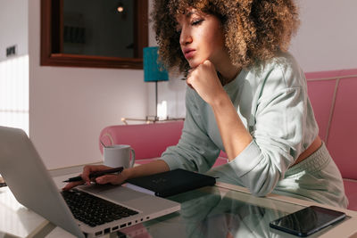 Focused african american female freelancer using netbook while sitting at table at home and working remotely on project