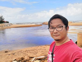 Portrait of young man wearing sunglasses at beach against sky