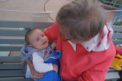 High angle view of grandmother holding baby while sitting on bench at park