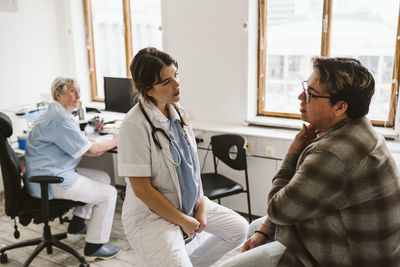 Female medical expert discussing with male patient while senior nurse sitting at desk