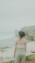 Rear view of woman standing at beach against sky