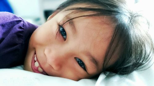 Close-up portrait of cute smiling girl lying on bed at home