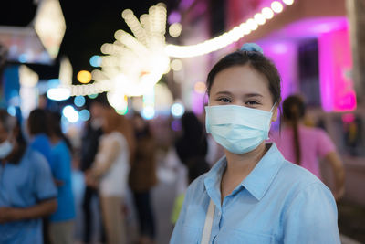 Asian women wearing masks go  event that is held at night. it  decorated with many light bulbs.