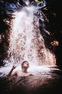 Shirtless woman swimming in river against waterfall