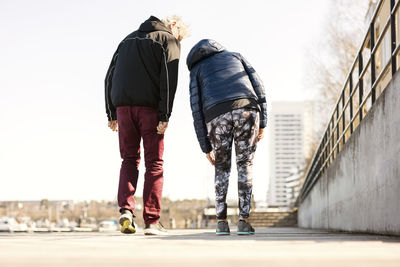 Rear view of senior couple in sportswear walking on sidewalk against clear sky