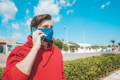 Portrait of young man holding camera against sky