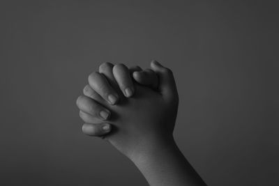 Cropped hands of child praying against gray background