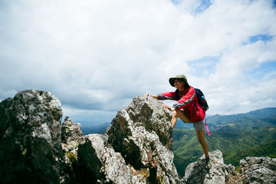 Side view of woman standing on rock against sky