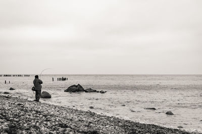 Side view of man fishing while standing at beach against sky