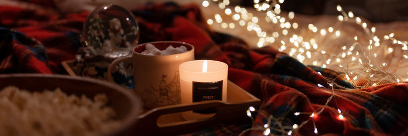 Cup of hot chocolate and marshmallows and candle on tray bed and glowing lights bokeh at home