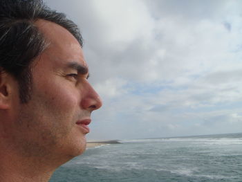 Side view of thoughtful man by sea against cloudy sky