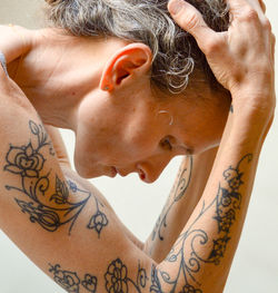 Close-up of tattooed woman with hand in hair against white background