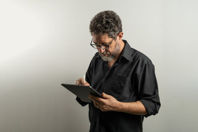 Man using digital tablet while standing against gray background