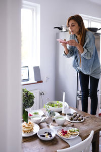 Blogger photographing food at table through mobile phone by window