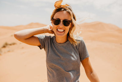 Portrait of young woman wearing sunglasses on sand at beach