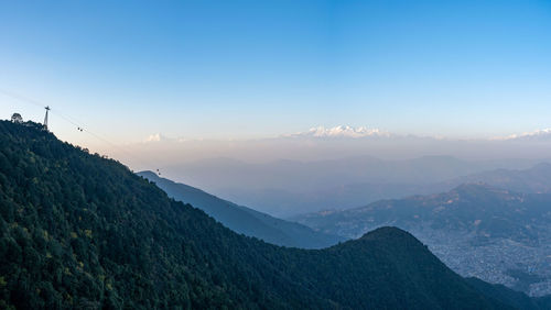 A panorama of cable cars going up and down a mountain with the himalayan mountain range