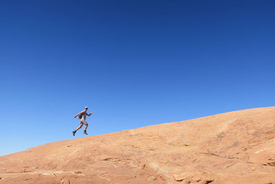 Low angle view of man running on desert against clear blue sky