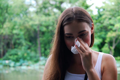 Beautiful young woman wiping sweat with tissue against trees