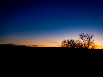 Silhouette trees on landscape against sky during sunset