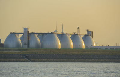 Factory by river against clear sky