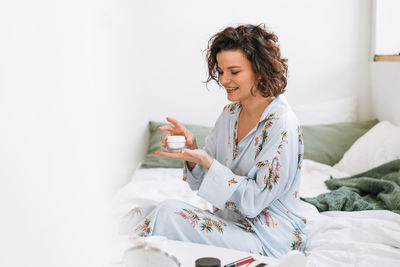 Young woman using mobile phone while sitting on bed at home