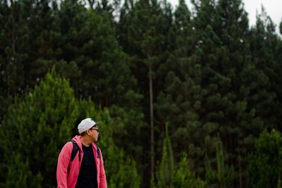 Young man looking away against trees