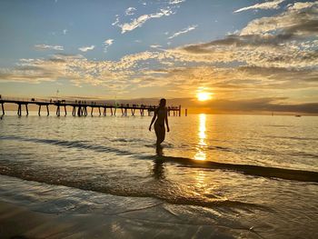 Silhouette woman standing on beach against sky during sunset