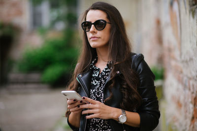 Young woman is thinking while waiting for a call on her smartphone.