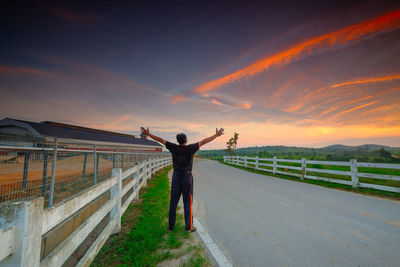 Rear view of man standing on road against sky during sunset