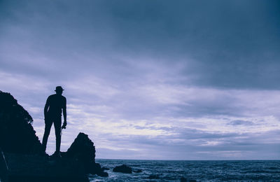 Silhouette man standing on rock by sea against sky