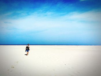 Full length rear view of man with backpack walking at beach against blue sky