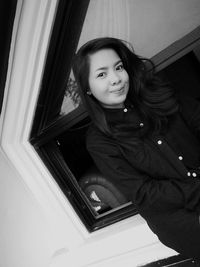 Portrait of smiling young woman standing against window